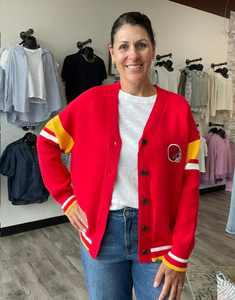 Red cardigan featuring a KC helmet on the front and Kansas City on the back. It has gold striping on the sleeves and hems.